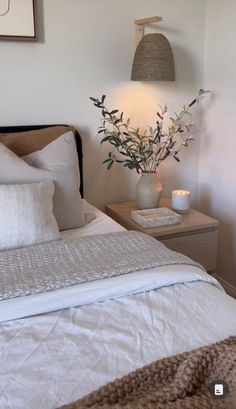 a bed with white sheets and pillows in a bedroom next to a vase filled with flowers