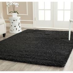 a black area rug on the floor in front of a white vase with flowers inside