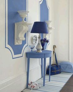 a blue table sitting next to a lamp on top of a wooden floor under a mirror