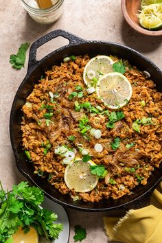 a skillet filled with rice, meat and cilantro garnished with sliced lemons