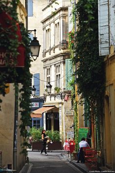 an alley way with people sitting at tables and walking down the street in front of tall buildings