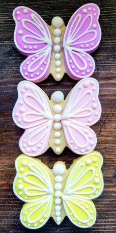 three decorated butterfly cookies sitting on top of a wooden table