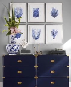 a blue and white dresser with four pictures on the wall above it, along with flowers