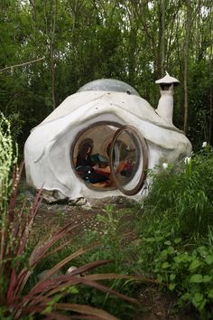 two people are sitting in the inside of a white structure surrounded by plants and trees