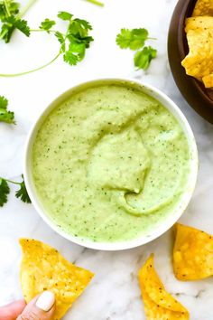 someone dipping guacamole into a bowl with tortilla chips