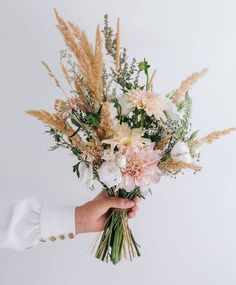 a person holding a bouquet of flowers in their hand with white and pink blooms on it