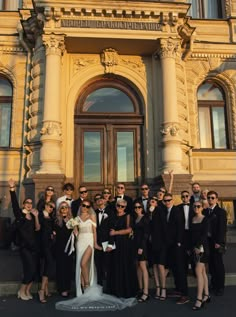 a group of people standing in front of a building posing for a photo with the bride and groom