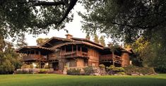 a large wooden house sitting in the middle of a lush green field next to trees