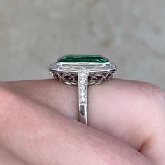 A bold ring featuring a 5.38 carat vivid green Zambian emerald. The center stone is surrounded by a halo of baguette-cut diamonds weighing 0.87 carats total. Adorning the shoulders are additional micro-pave set round brilliant cut diamonds weighing approximately 0.14 total. This ring is handcrafted in platinum. This ring is certified.
The measurements of this ring including the halo are approximately 16.78mm x 12.86mm. The approximate measurements of the emerald are 12.44mm x 8.12mm.
The current Luxury Octagon Gia Certified Emerald Ring, Large Stone Ring Settings, Luxury Dazzling Emerald Ring With Halo Design, Vintage Diamond Earrings, Asscher Cut Ring, Kunzite Ring, Fancy Diamond Ring, Rose Cut Ring, Large Stone Rings