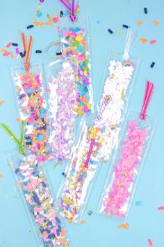 three plastic straws filled with confetti and sprinkles on a blue surface