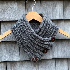 a gray knitted cowl hanging from a wooden hanger on the side of a building