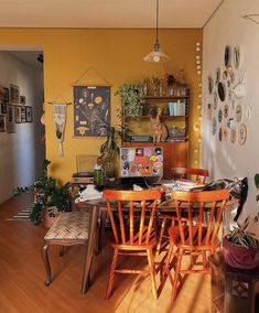 a dining room with yellow walls and orange chairs in front of a wooden table surrounded by potted plants