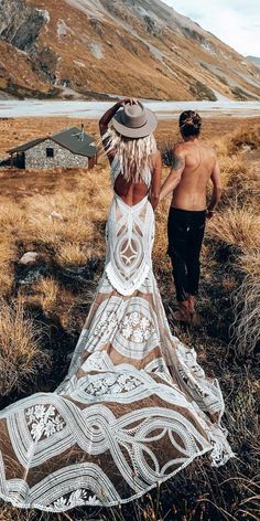 a man and woman are walking in the grass together, with mountains in the background