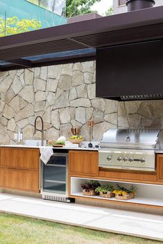 an outdoor kitchen with stainless steel appliances and wood cabinets, built into the side of a stone wall