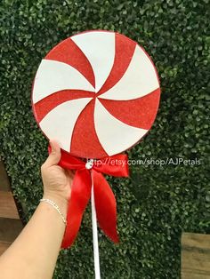 a hand holding a lollipop in front of a green wall with red and white stripes