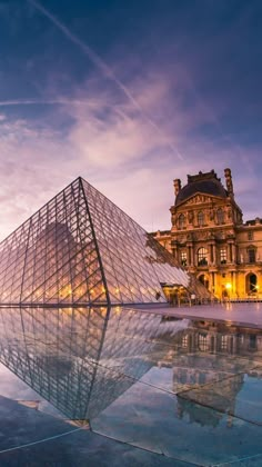 a large glass pyramid in front of a building with a reflection on the ground at dusk