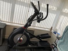 an exercise bike sitting in front of a window next to a trash can and microwave