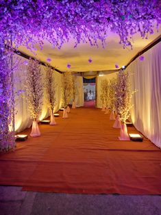 an aisle decorated with purple flowers and white drapes