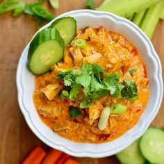 a white bowl filled with food next to cucumbers and carrots on top of a wooden table