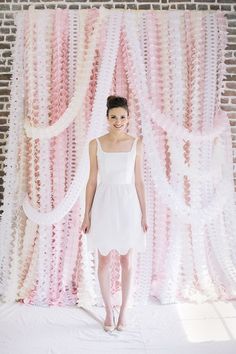 a woman standing in front of a backdrop with pink and white streamers on it