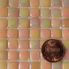 a penny sitting on top of a white tile floor with pink and purple tiles in the background