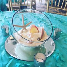 a table topped with a glass bowl filled with sand and starfish on top of it