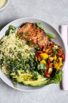 a white plate topped with meat and vegetables next to a bowl of rice, avocado