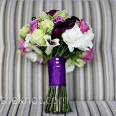 a purple vase filled with lots of flowers on top of a striped couch next to a pillow