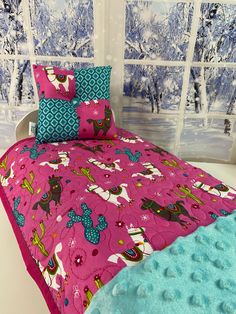 a bed covered in pink and blue sheets next to a window with snow outside it