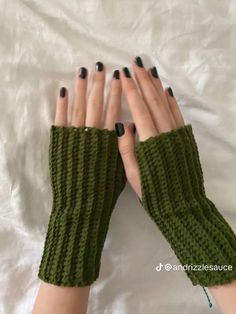 a woman's hands with black fingernails and green knitted gloves on top of a white sheet