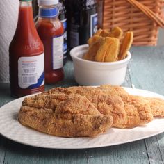 two fried fish fillets on a white plate next to ketchup bottles