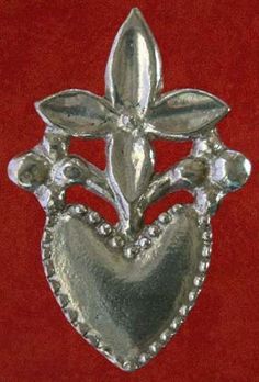 a silver brooch that is on a red cloth with beads and leaves in the shape of a heart