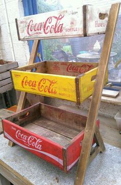 an old coca - cola crate is sitting on top of a wooden shelf with two soda cans in it