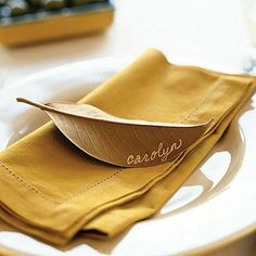 a wooden spoon sitting on top of a yellow napkin next to a white plate with a brown leaf