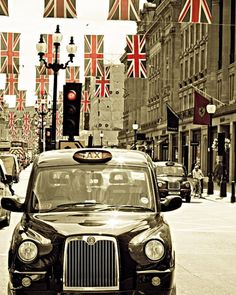 a taxi cab driving down a street next to tall buildings with union jack flags hanging from it's roof