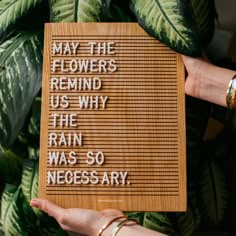 a person holding up a wooden sign that says may the flowers remind us why the rain was so necessary