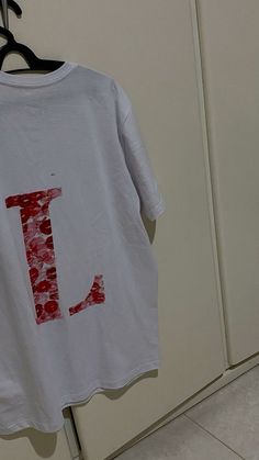 a white t - shirt with the letter j on it hanging from a clothes rack