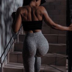 a woman in grey leggings and black top walking up stairs with her back to the camera