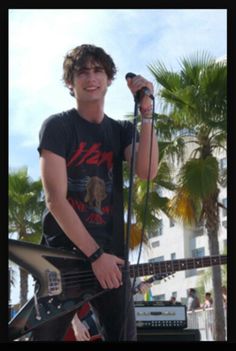 a young man holding a guitar while standing in front of a microphone and some palm trees