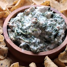 a wooden bowl filled with spinach dip surrounded by chips