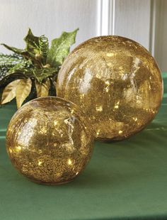 two shiny gold balls sitting on top of a green table next to a potted plant