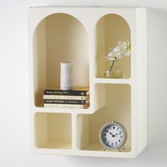 a clock and some books on a shelf with a white wall in the back ground