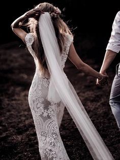 a woman in a wedding dress holding the hand of a man who is wearing a veil