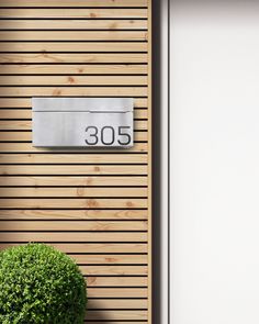 a house number sign on a wooden wall next to a potted plant and door