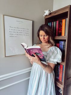 a woman standing in front of a bookshelf holding a book