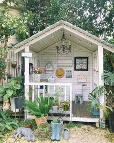 a small white shed with potted plants on the front porch and an outdoor kitchen