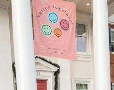 a pink banner hanging from the side of a white building with smiling faces on it