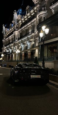 a black sports car is parked in front of a building at night with its lights on