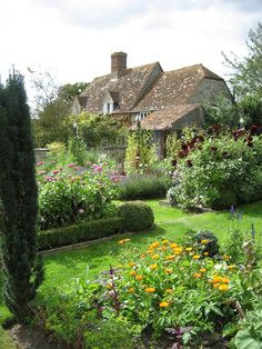 the garden is full of colorful flowers and plants in front of an old brick house