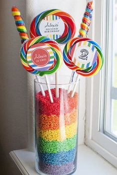 rainbow rice lollipops in a clear glass with candy sticks sticking out of it